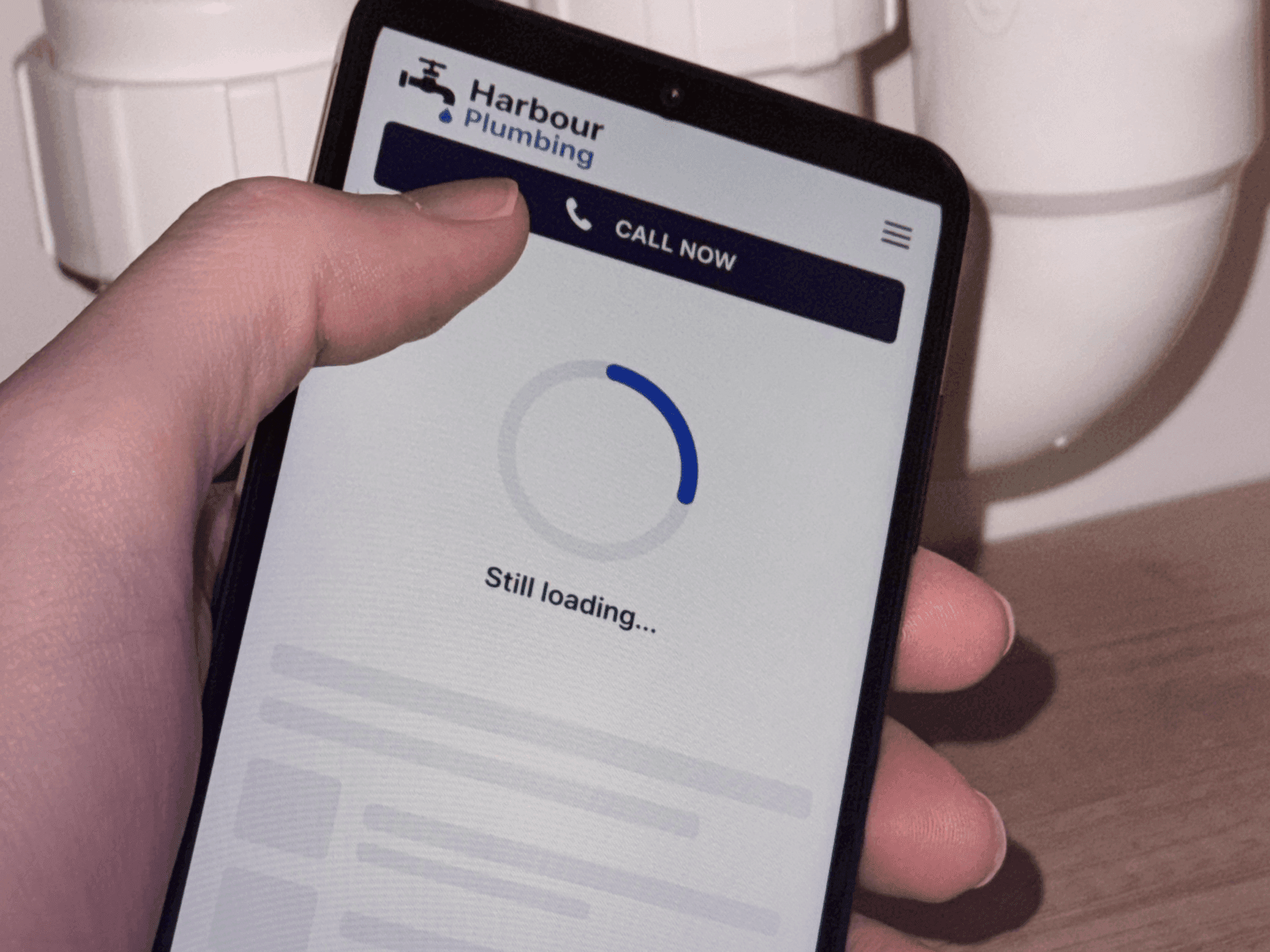 Plumber's website stuck on a loading spinner on a phone held under a leaking sink