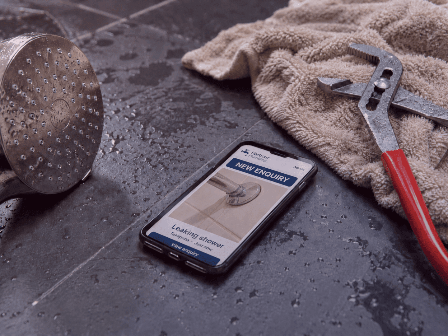 New enquiry for a leaking shower in Takapuna on a phone beside a shower head and pliers