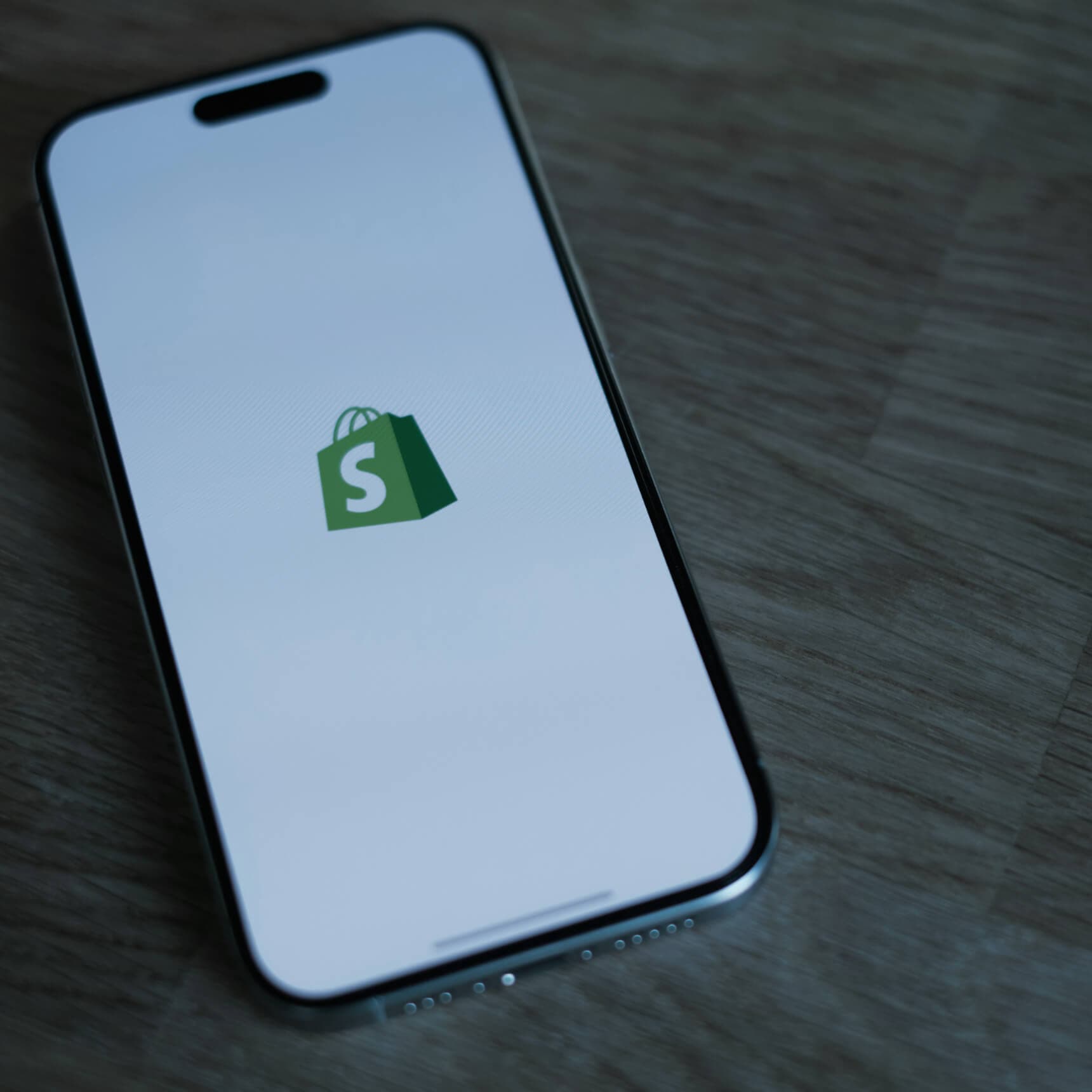 A smartphone showing the Shopify shopping-bag logo, lying on a wooden desk
