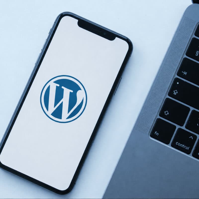 A smartphone showing the WordPress logo, on a desk beside a laptop keyboard