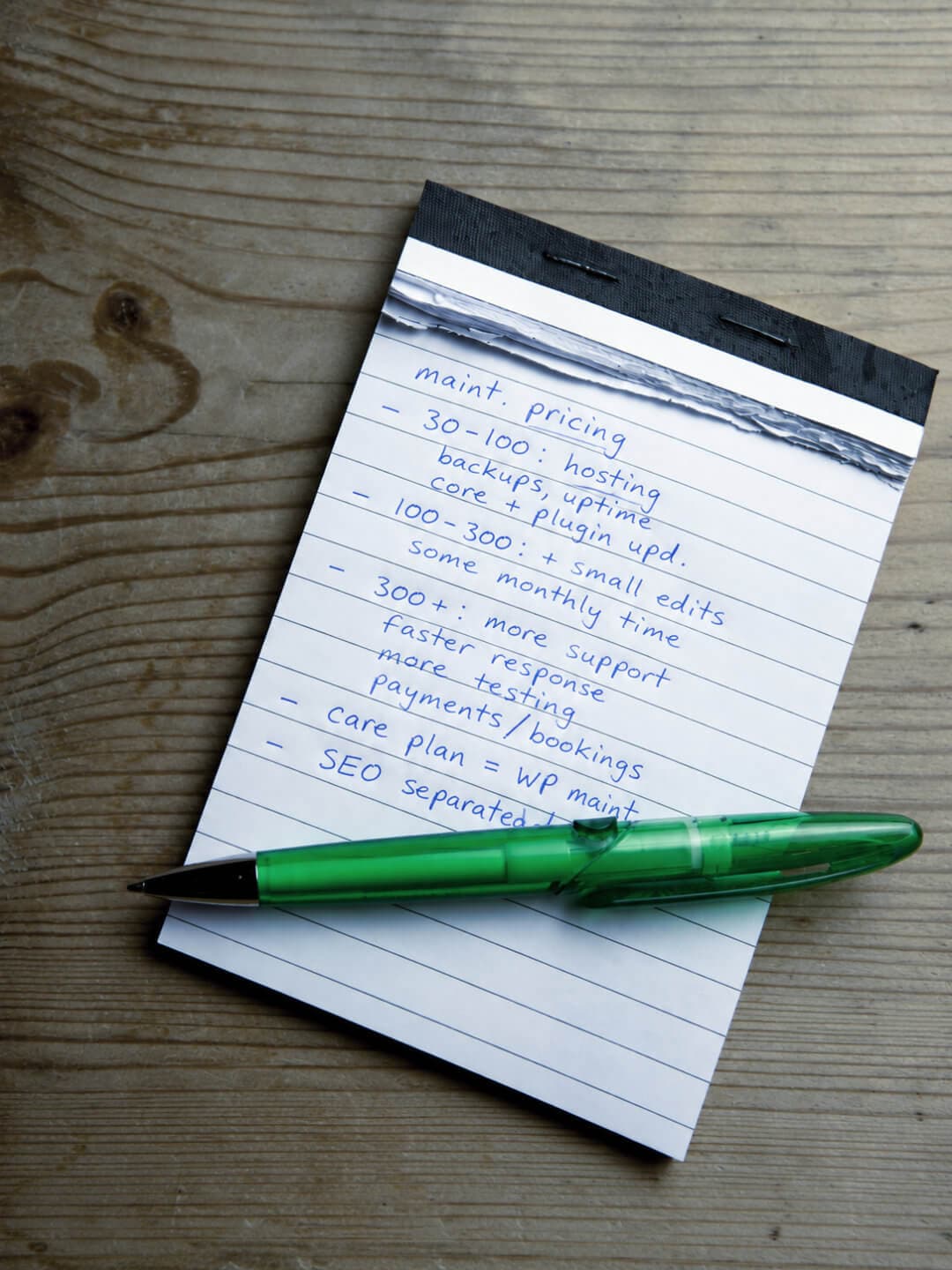 Handwritten website maintenance pricing notes with a green pen on a notepad