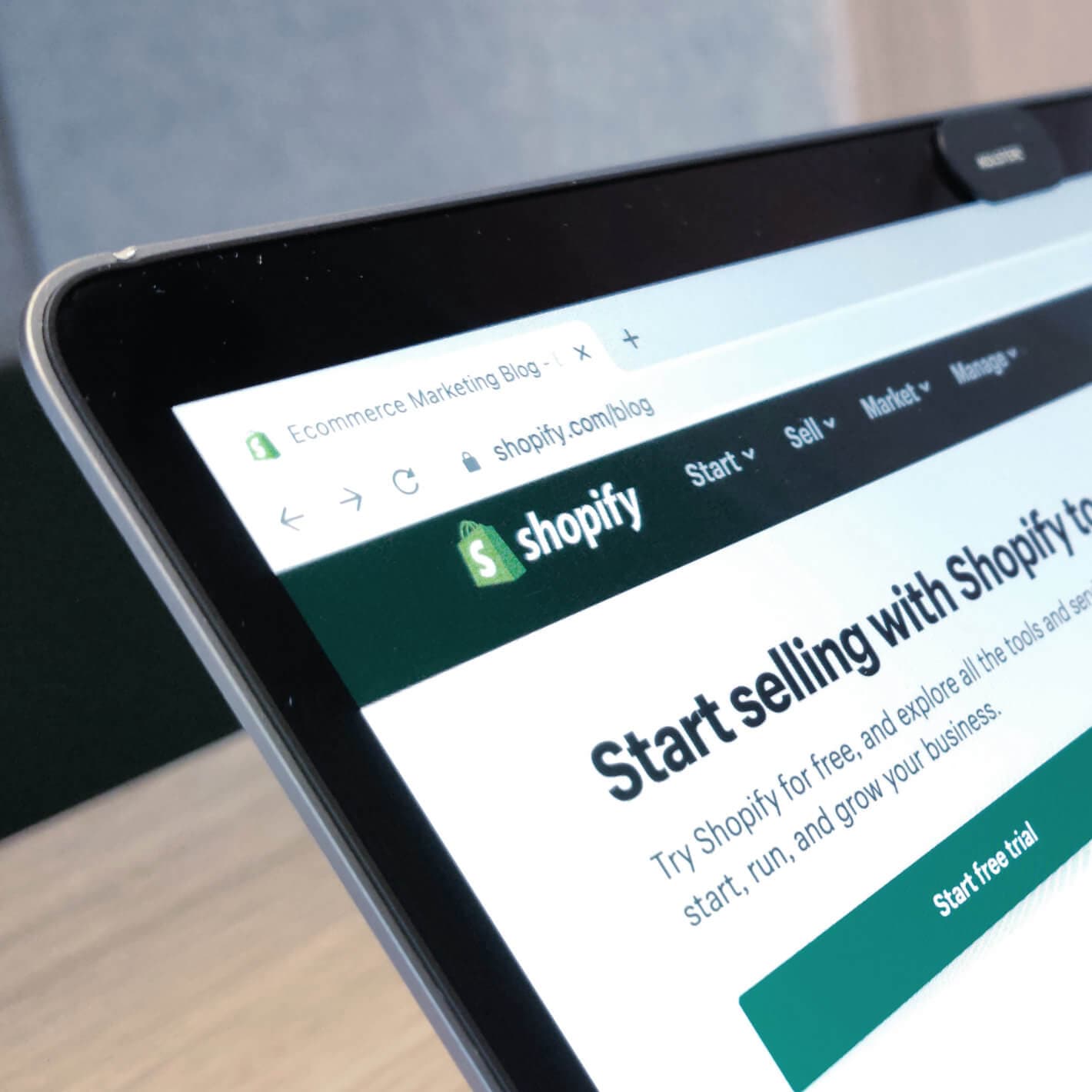 Close-up of a laptop screen showing the Shopify website with its "Start selling with Shopify" banner