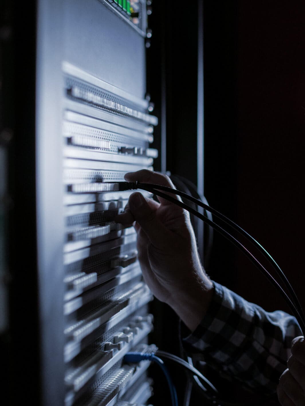 A hand plugging a network cable into a server rack in a dimly lit room