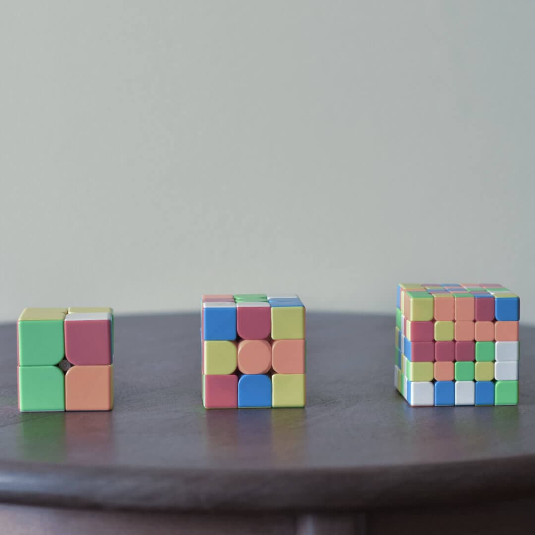 Three puzzle cubes of increasing size side by side on a wooden table